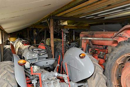 Een schuur vol grijze Fergusons en rode Massey-Fergusons met rechts de grote MF Super 90 uit 1962
